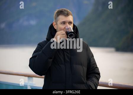 Man drinking coffee from a clear glass while relaxing on a ship deck Stock Photo