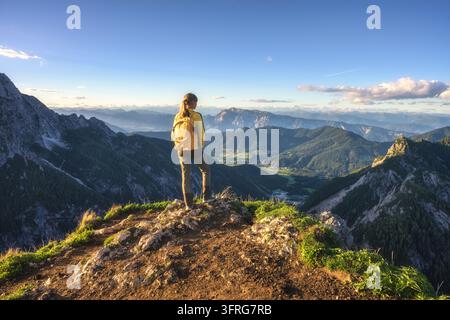 Woman with yellow backpack standing on rocky mountain summit Stock Photo