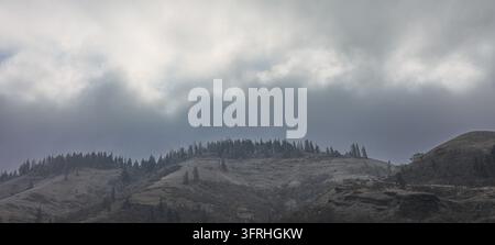 Dark Storm Clouds Rolling Over Dusting of Snow on Pacific Northwest Hillside Stock Photo