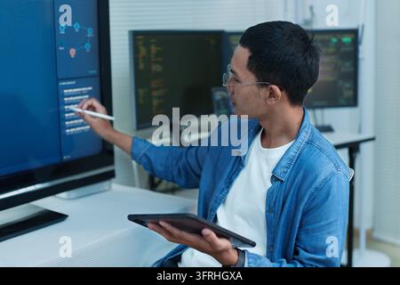 Software developer using a stylus and tablet while analyzing programming code and digital data on multiple computer screens. Stock Photo