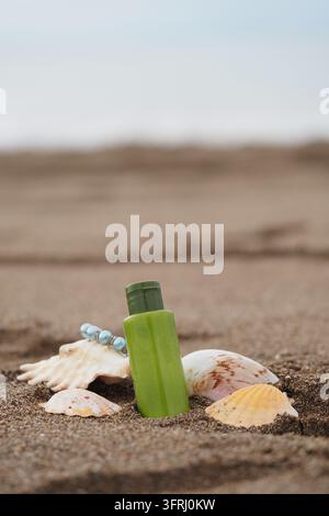 a green plastic bottle of lotion surrounded by seashells on a sandy beach Stock Photo