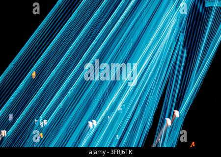 Glowing cyan and turquoise light trails sweep diagonally across black night scene with white and orange flares, long exposure technique. Digital speed Stock Photo