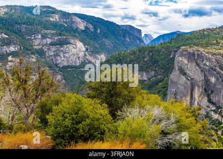 Scenic view featuring Half Dome framed between El Capitan and surrounding forested ridges beneath a partly cloudy blue sky in Yosemite National Park, Stock Photo