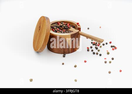Round wooden spice container filled with mixed black green red peppercorns and small wooden spoon on white background, rustic food Stock Photo