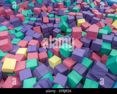 Foam pit filled with scattered purple, pink, turquoise and yellow padded cubes Stock Photo