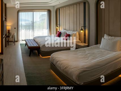 Fethiye, Turkey - 8 October 2025: XO Cape Arnna hotel room in Fethiye with two large beds, red pillows, an upholstered bench and a glass door to the b Stock Photo