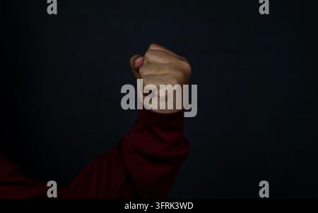 A strongly clenched human fist is held high and straight upward against a solid black background, conveying a powerful message of unity, resistance, a Stock Photo