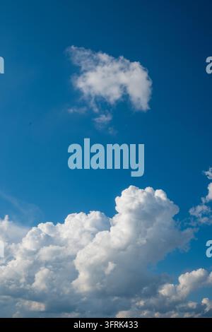 A vertical view of a deep blue sky with a single white cloud floating in the upper center and larger cumulus clouds at the bottom. The sky is clear Stock Photo