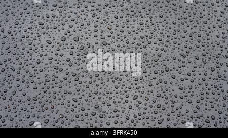 Close-up of a metallic surface covered with water droplets, creating an abstract texture with reflective highlights and subtle variations in light. Th Stock Photo