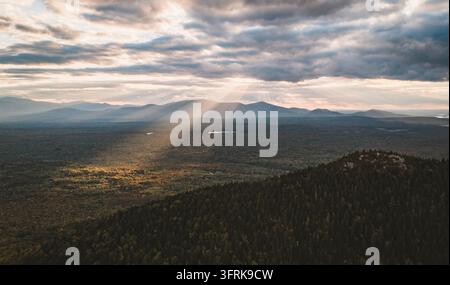Sunlight breaking through dramatic clouds over forest hills Stock Photo