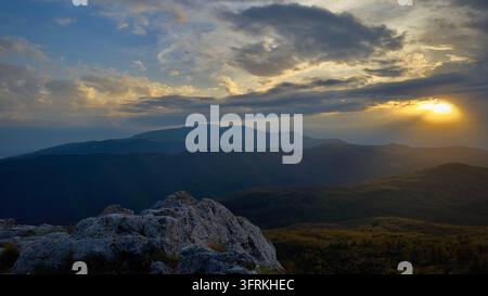 Golden sunset over layered mountain ranges with rocky foreground Stock Photo