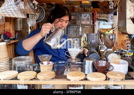 Vendor hand-brews drip coffee with a gooseneck kettle and ceramic filter cone at an outdoor coffee stand in Tokyo Japan, with jars of bean Stock Photo