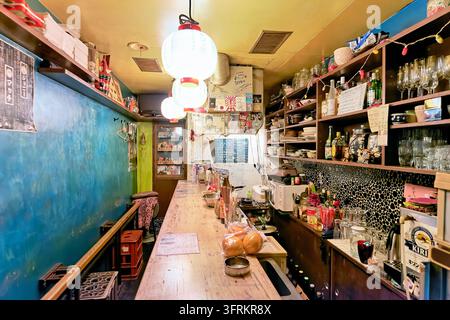 Long wooden counter lined with paper lanterns, shelves of liquor bottles, glassware and handwritten menus inside a tiny drinking spot in Japan. Stock Photo