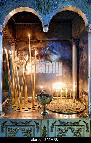 Beeswax taper candles burning in a brass holder and a sand tray at an ornate metal candle stand inside a Greek Orthodox church Stock Photo