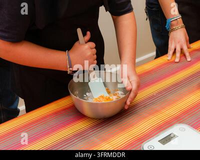Two people preparing food mixing a bowl of ingredients on a striped tablecloth. Stock Photo