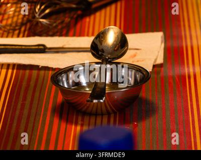 A stainless steel bowl with a ladle placed inside on a striped tablecloth. Stock Photo