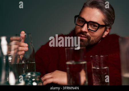 Handsome man in fashionable attire relaxes with glasses of clear beverages nearby. Stock Photo