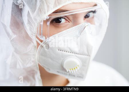 Portrait of beautiful caucasian young female medical laboratory worker, closing eyes full of fear, wearing goggles, overalls, N95 face mask, looking a Stock Photo