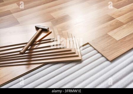 Installing laminated floor, detail on pile of wooden tiles, hammer and pencil, over white foam base layer Stock Photo