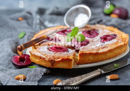 Cut homemade pie with red plum and almond cream on the table with dark homespun cloth, selective focus Stock Photo