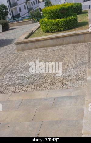 Artistic Calçada Portuguesa pavement showing the town crest in Carrazedo de Montenegro, Valpaços, framed by green hedges and stone steps, Portugal. Stock Photo