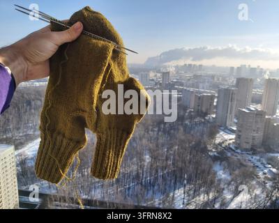Person is holding a pair of knit gloves. The gloves are green and have a lot of yarn on them over city buildings Stock Photo