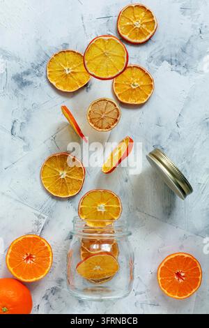 Glass jar, dried orange and lemon slices, fresh tangerines on white stone background Stock Photo