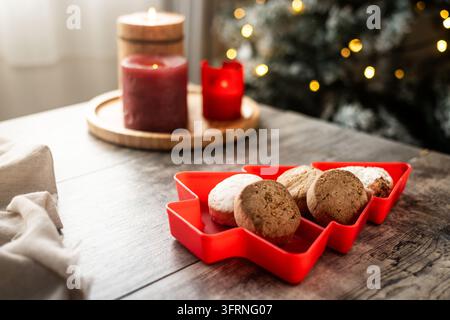 Close-up of traditional Spanish polvoron cookies arranged in a red Christmas tree dish, with assorted shortbread, glowing candles, festive lights, and Stock Photo