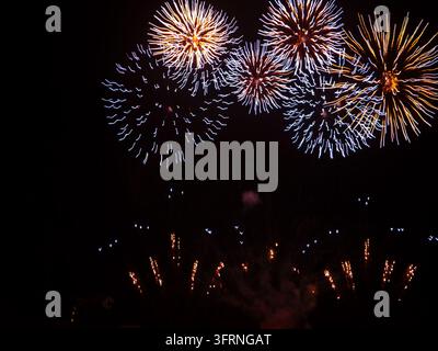 Colorful fireworks burst in bright orange, gold, and blue trails against a deep black night sky, creating a festive celebration display with glowing s Stock Photo