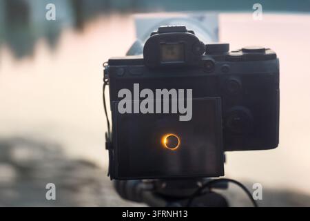 Rear view of a digital camera displaying a glowing solar eclipse on its screen outdoors in Spain, with soft sunset light and a blurred natural backgro Stock Photo