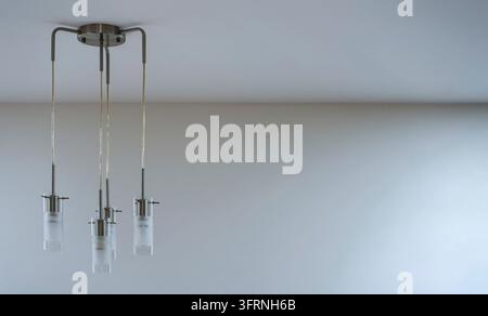 Modern metal and glass lamp with four lights hanging form the ceiling, empty space right side Stock Photo