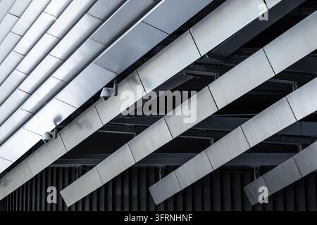 Close-up abstract view of a contemporary skyscraper structure, featuring overlapping silver metal panels, diagonal lines, dark shadows, and repeating Stock Photo