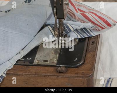 Close-up of an old mechanical sewing machine with presser foot and needle positioned over striped white fabric, showing traditional textile work and t Stock Photo