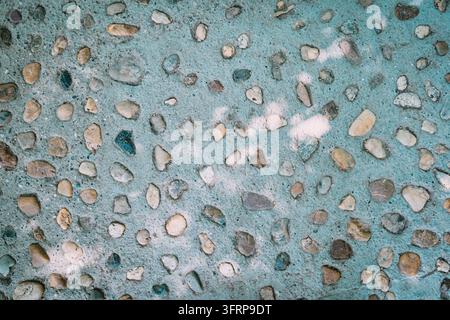 Pebble aggregate concrete surface with mixed stones embedded in teal cement - texture background. Stock Photo