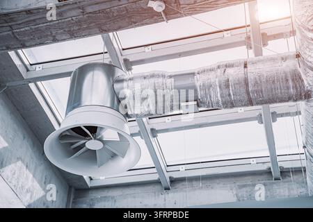 Industrial ventilation system with fan and insulated ductwork hanging from a modern building ceiling, ensuring air circulation and climate control Stock Photo