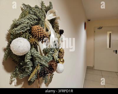 Beautiful wreath made of pine cones and gold balls is hanging on a wall with a lovely decoration for the room and adds a touch of warmth and coziness to space entrance of the residential complex floor Stock Photo