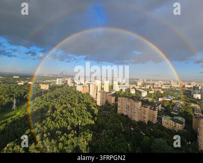 Rainbow is seen in the sky above a city. The rainbow is very large and spans the entire sky Stock Photo