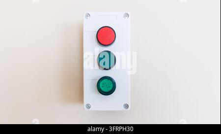 White plastic control box features red and green push buttons mounted on light wall surface. Industrial equipment interface, electrical automation, an Stock Photo