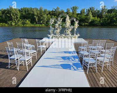 White wedding ceremony is taking place on a wooden deck. The chairs are arranged in rows, and the bride and groom are standing in the center of the ceremony empty interior Stock Photo