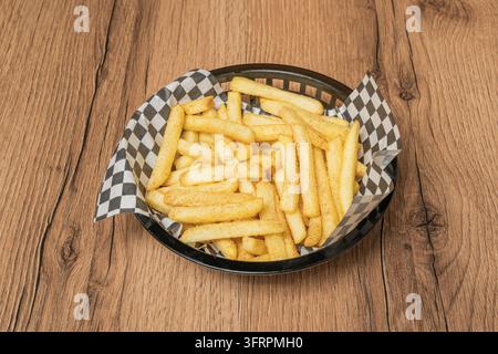 Seasoned french fries stacked in a round black basket with black-and-white checkered wax paper on a wooden surface. Stock Photo