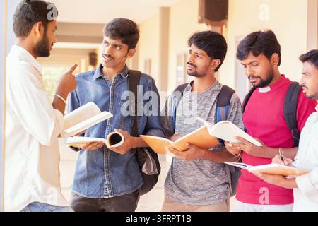Group of students listening to senior student to settle doubt - young smart man explaining to his classmates by putting in books at college - educatio Stock Photo