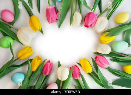 A vibrant Easter floral frame featuring fresh pink, yellow, and white tulips paired with colorful painted eggs. The elements are arranged in a circula Stock Photo