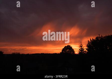 Sunset sky with clouds in the form of flames. Bright orange rays illuminate dark dramatic cloudy sunrise. Nature silhouette, colorful dawn view Stock Photo
