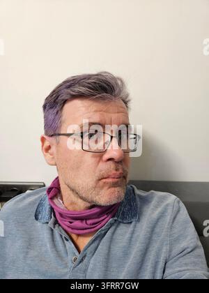 Man with purple hair and glasses. He is wearing a blue shirt and a purple scarf. He is looking at the camera Stock Photo