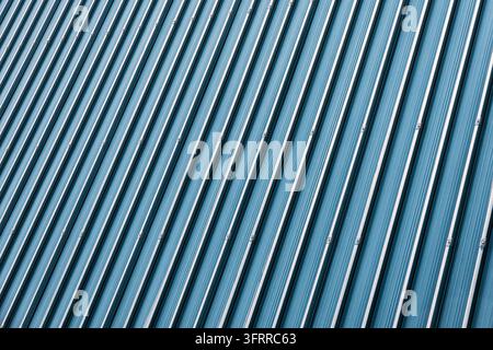 Blue corrugated metal siding forming a striking diagonal pattern and texture. Industrial building facade with parallel lines Stock Photo