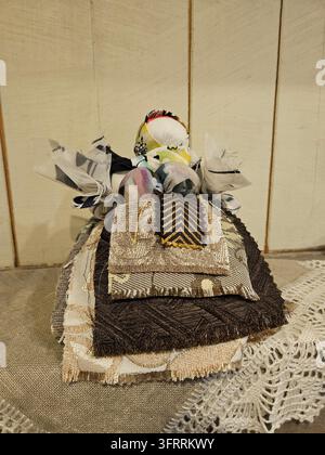 MINSK - MAR 25, 2025: A doll made of fabric and lace is sitting on a table. The doll is dressed in a variety of colors and patterns, and it is a handmade piece. Stock Photo