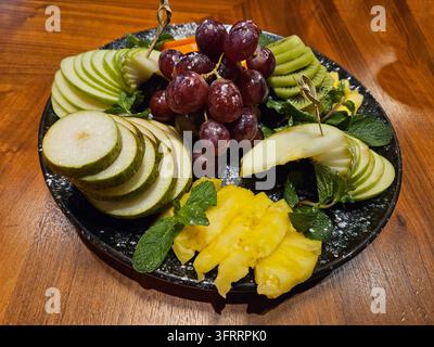 A plate of fruit with a variety of apples, pears, and grapes. The plate with pear, kiwi is on a wooden table Stock Photo