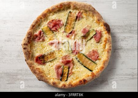 Italian white pizza topped with cooked ham, melted mozzarella and grilled zucchini, photographed from above on a rustic wooden surface. Stock Photo