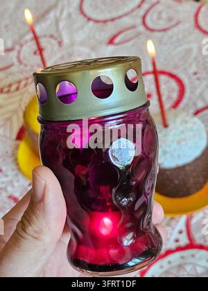 Hand holding a purple candle holder with a lit candle. There is a cake with candles on it in the background Stock Photo