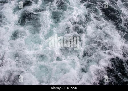Close-up view of a ship's wake showing white foam and turbulent water against dark ocean waves. Churning surface of the sea created by a moving vessel. Stock Photo